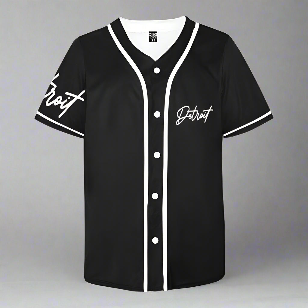 Black short-sleeve baseball jersey laid flat against a gray background. The jersey features white piping along the collar, button placket, and sleeves, with white buttons down the front. The word 'Detroit' is printed in a stylish cursive font on the left chest and also on the right sleeve."