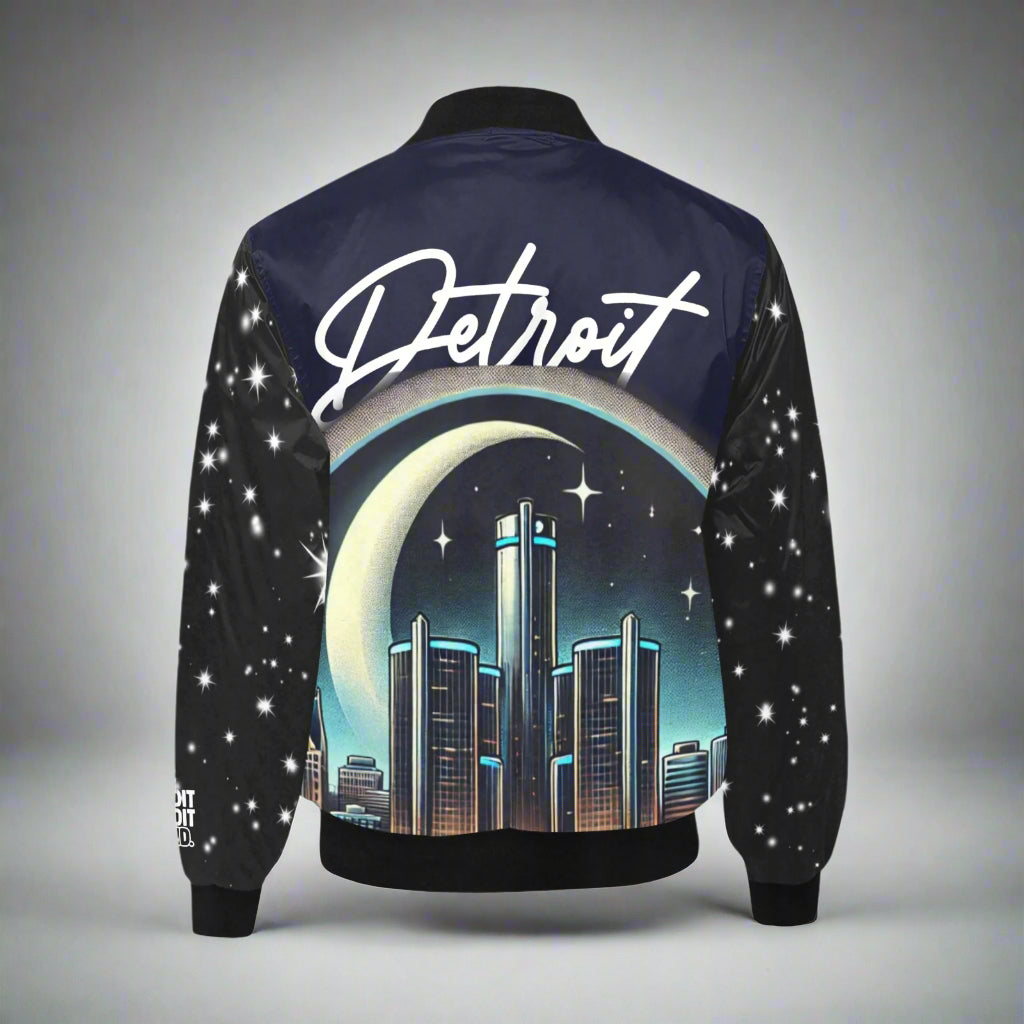 Detroit-themed bomber jacket displayed flat against a gray background. The back of the jacket features a large graphic of the Detroit skyline under a crescent moon and starry night sky. The word 'Detroit' is written in large white cursive lettering across the top. The sleeves are black with scattered white star designs, and the jacket includes black ribbed cuffs, collar, and waistband."