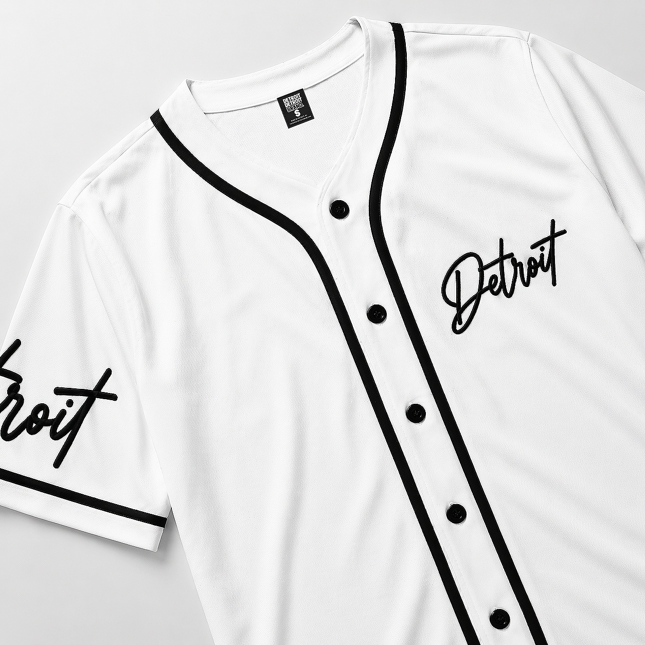 Close-up of white Detroit baseball jersey with black piping, button front, and embroidered Detroit script logo on chest