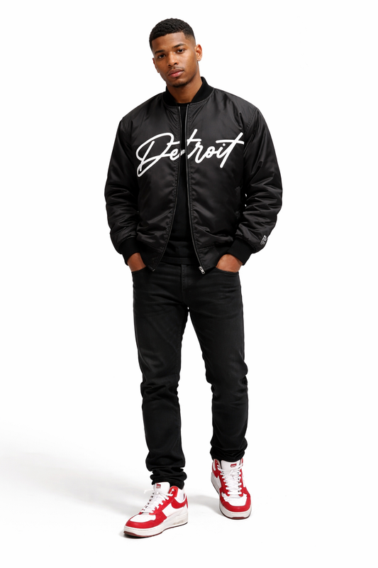 Man wearing a black bomber jacket with 'Detroit' text, black pants, and red and white sneakers on a white background