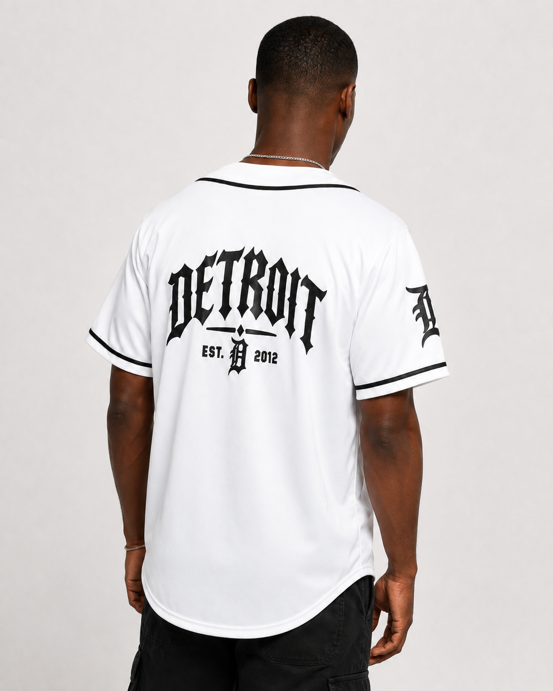 A man viewed from the back wearing a white Detroit Tigers baseball-style jersey with black trim and a large black 'DETROIT EST. D.
