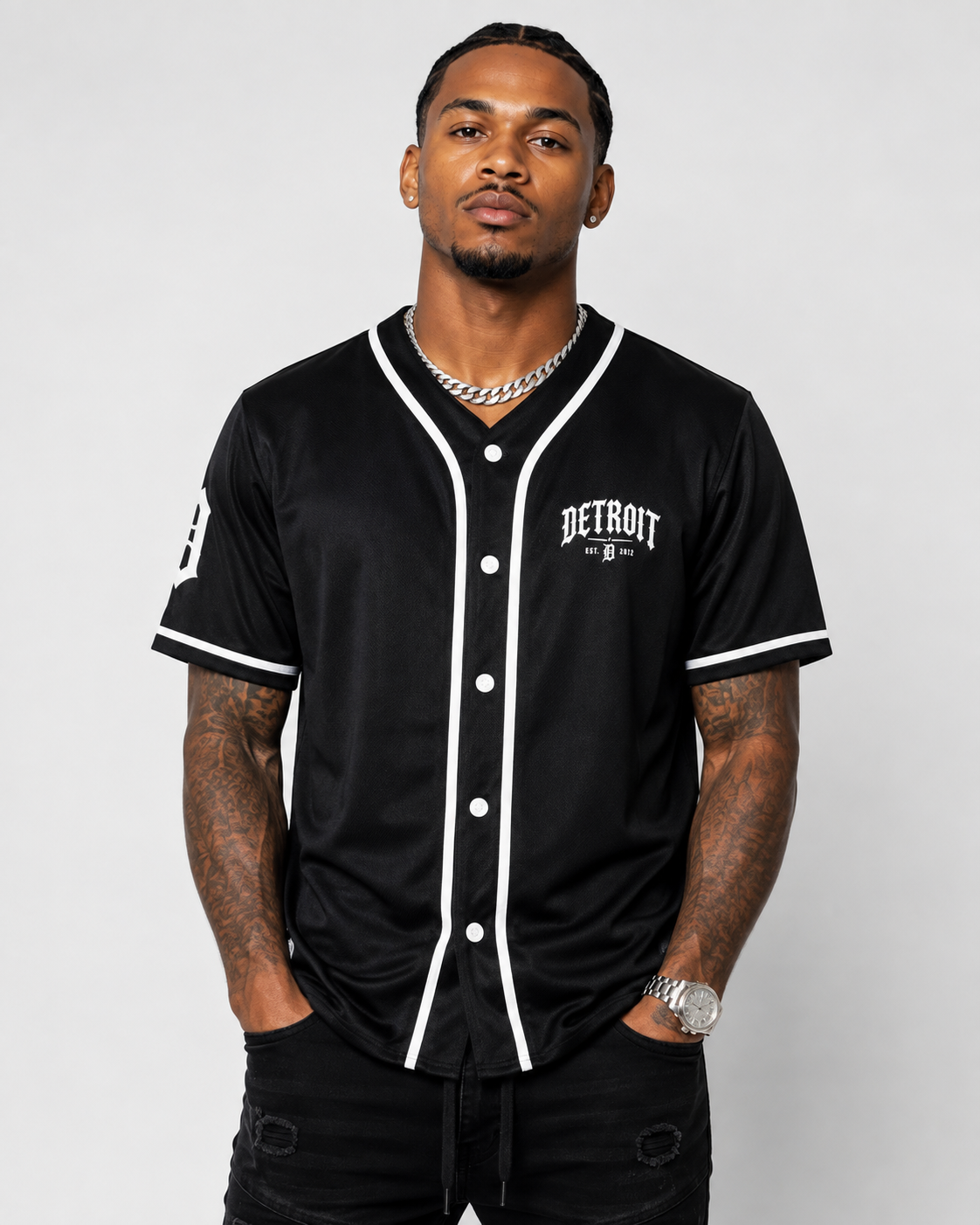 A man wearing a black Detroit Tigers baseball-style jersey with white trim and buttons, standing against a light gray studio background.