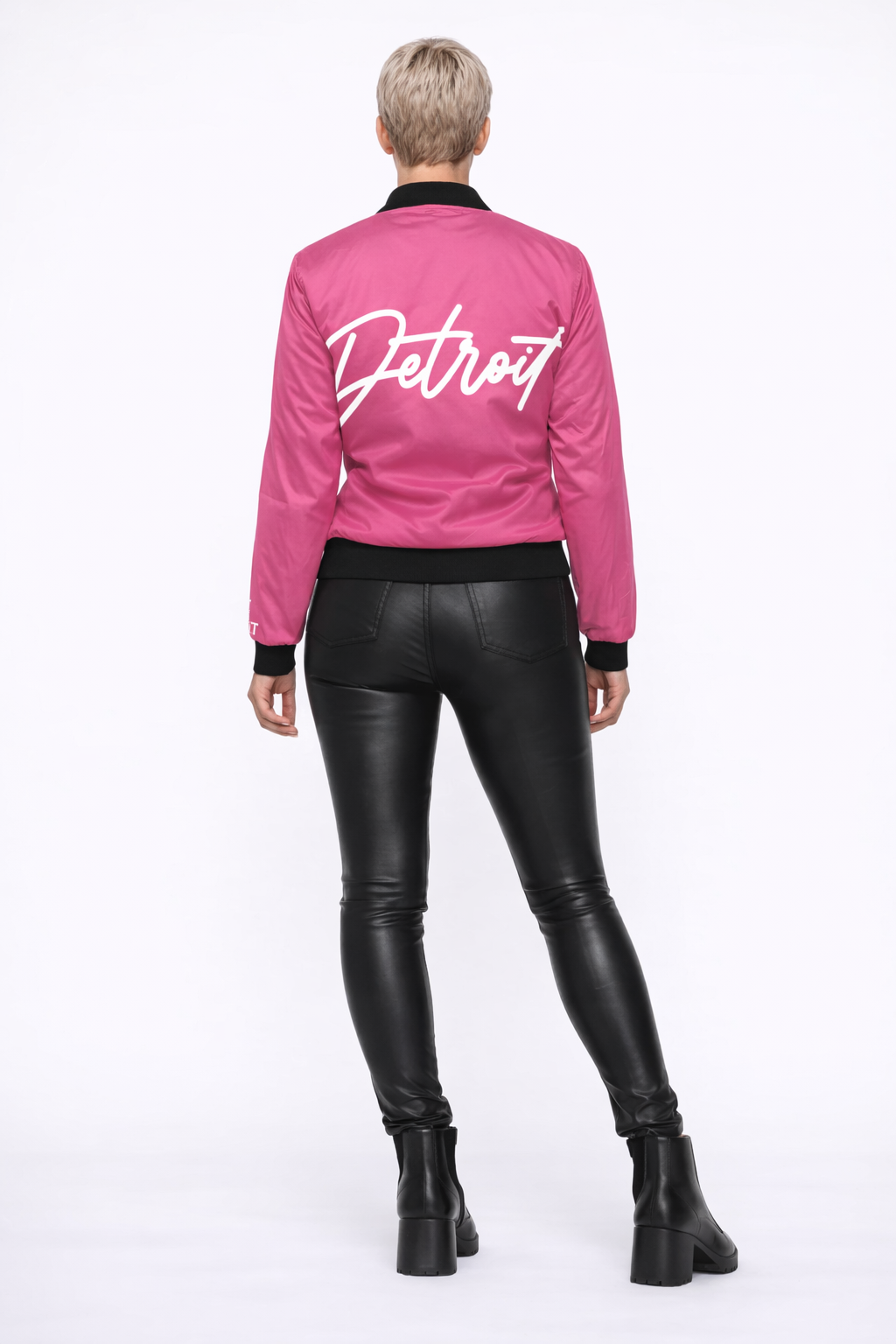 Person wearing a pink jacket with 'Detroit' text and black leather pants on a white background
