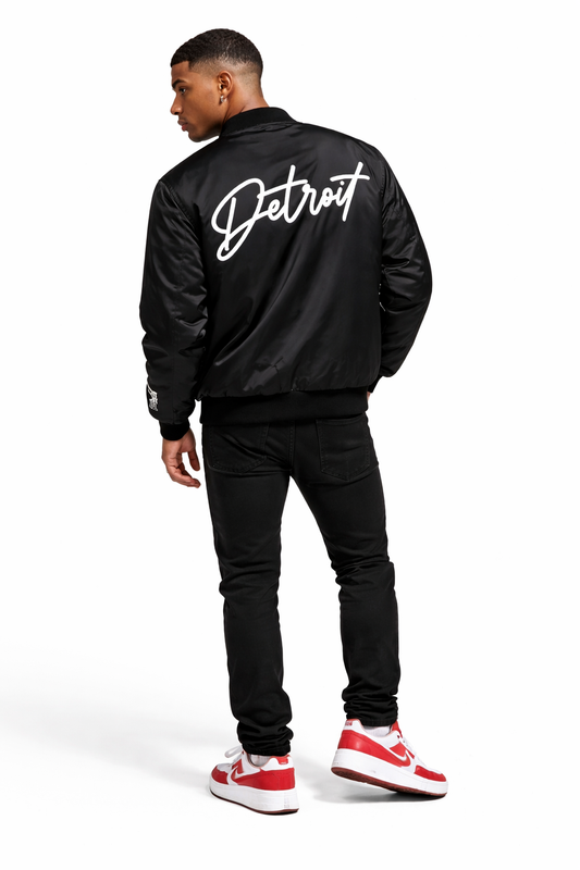 Person wearing a black jacket with 'Detroit' written on the back, standing against a white background.