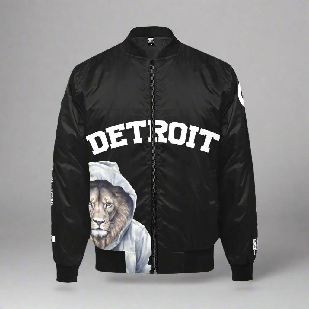 Black bomber jacket displayed flat against a gray background. The front features the word 'DETROIT' in bold white capital letters across the chest. Below the text, there is a graphic of a lion wearing a white hoodie. The jacket has a black zipper, ribbed cuffs, collar, and waistband. Additional 'DETROIT' text designs appear on the sleeves