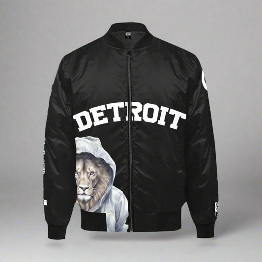 Black bomber jacket displayed flat against a gray background. The front features the word 'DETROIT' in bold white capital letters across the chest. Below the text, there is a graphic of a lion wearing a white hoodie. The jacket has a black zipper, ribbed cuffs, collar, and waistband. Additional 'DETROIT' text designs appear on the sleeves
