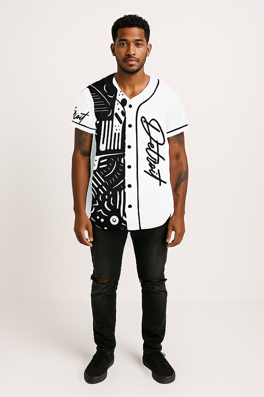 A man standing against a light-colored background, wearing a black and white baseball-style jersey with a bold abstract design on the left side and solid white on the right side. The jersey features black piping, front buttons, and the word 'Detroit' written in a cursive font on the right chest and left sleeve. He is also wearing ripped black jeans and black sneakers