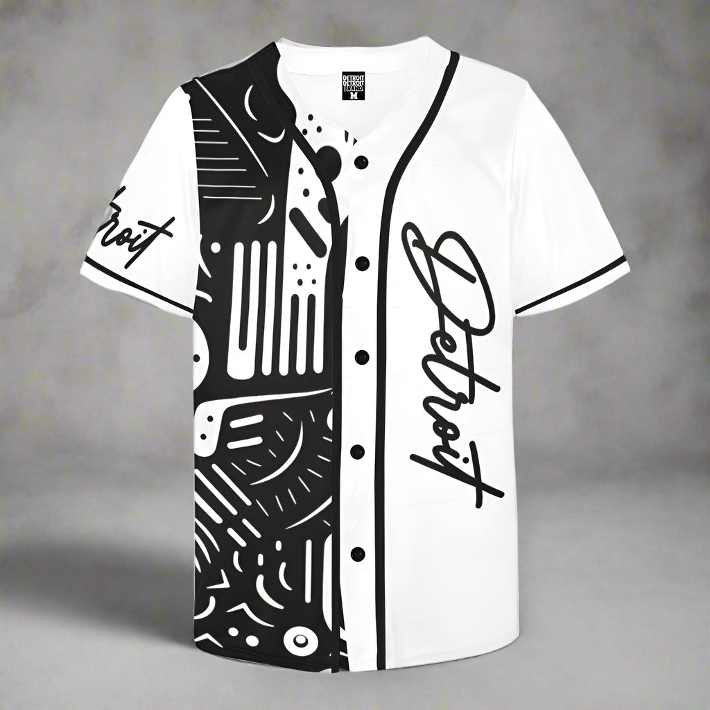 White short-sleeve baseball jersey displayed flat against a gray background. The jersey features black buttons and black piping along the collar, front placket, and sleeves. The right side displays the word 'Detroit' in a large cursive font, while the left side features a bold black abstract pattern with various lines, shapes, and dots. The word 'Detroit' is also printed in cursive on the left sleeve