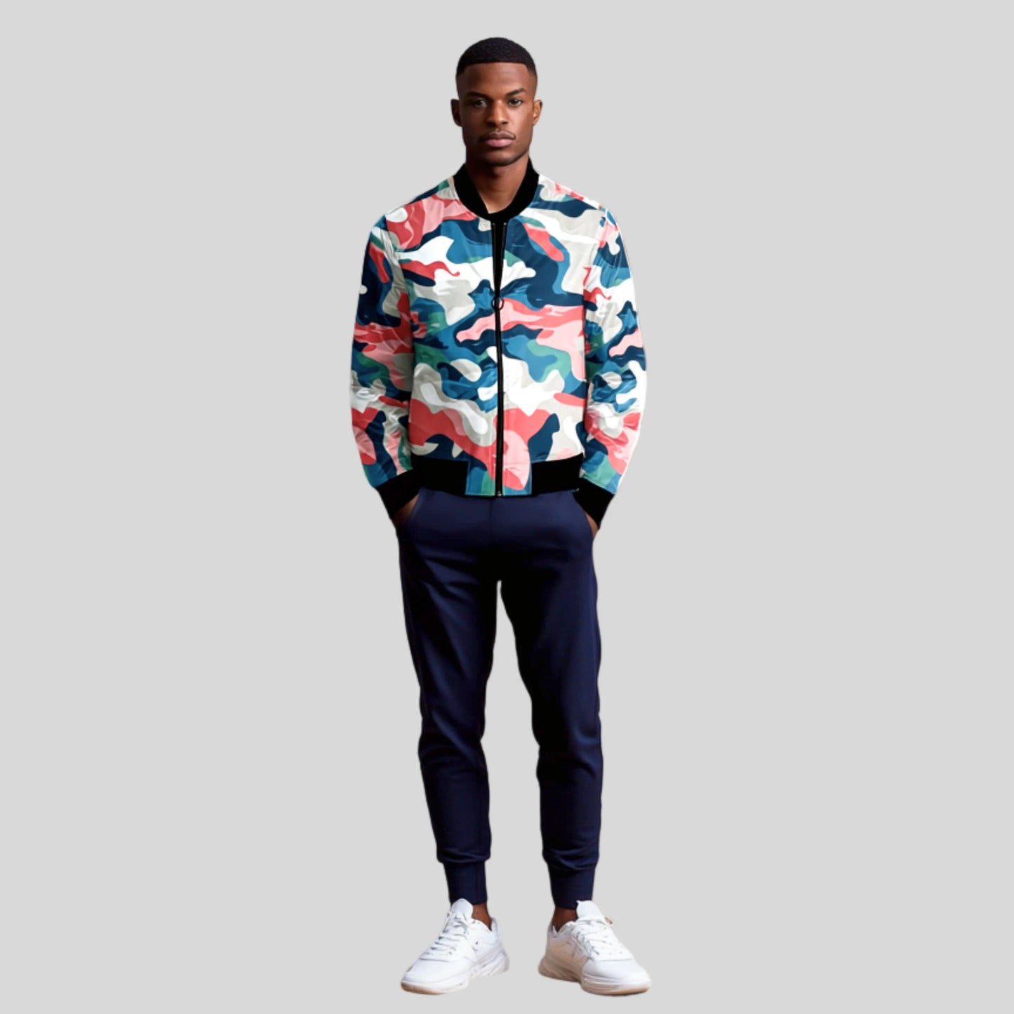 Man wearing a colorful camo bomber jacket in shades of blue, pink, white, and teal, paired with dark joggers and white sneakers, standing against a gray background.
