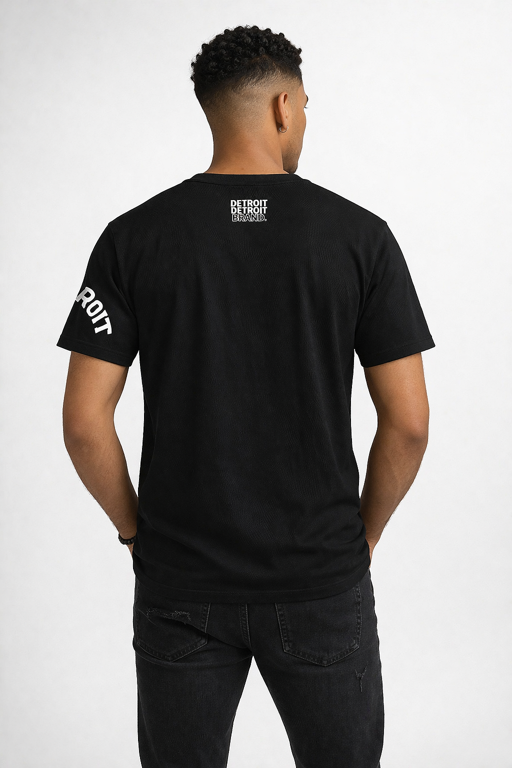 Back view of male model wearing black Detroit 313 t-shirt with Detroit Detroit Brand logo on upper back in urban street setting