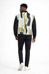 Back view of dark skinned male model wearing Detroit abstract bomber jacket with multicolor art panel, black turtleneck, slim fit black trousers, and clean white Armani Exchange sneakers on a white studio background