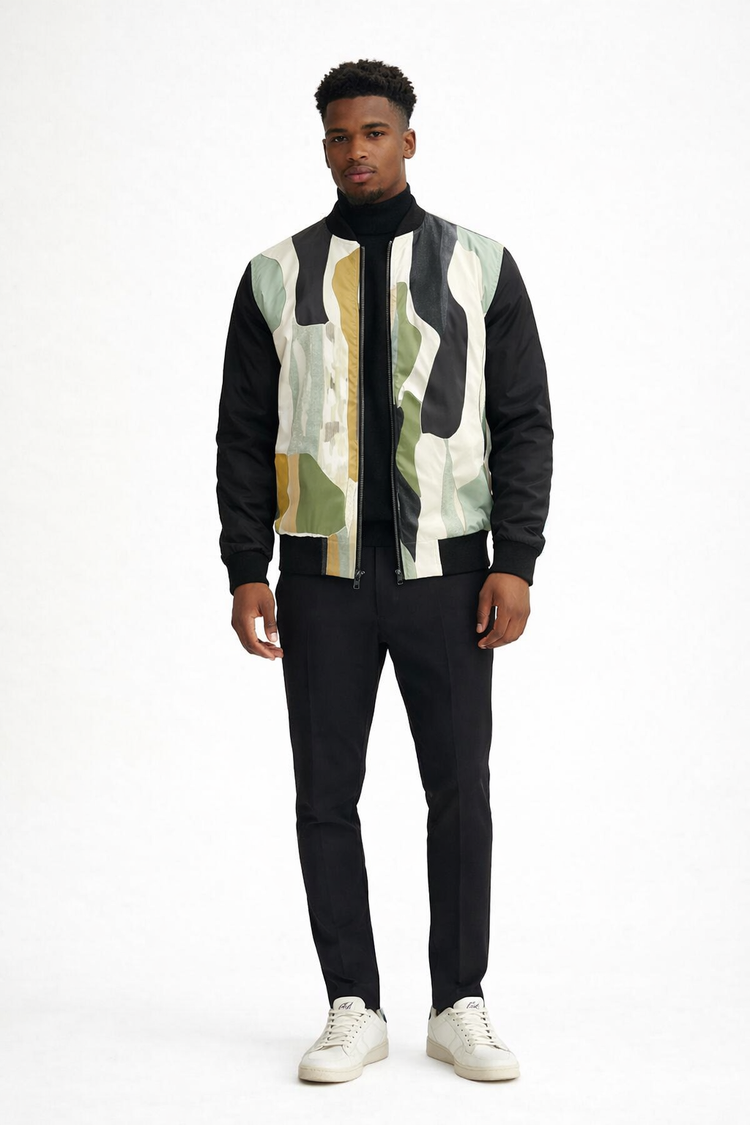 Dark skinned male model wearing a Detroit abstract bomber jacket over a black turtleneck with slim fit black trousers and white Armani Exchange sneakers in a clean white studio setting