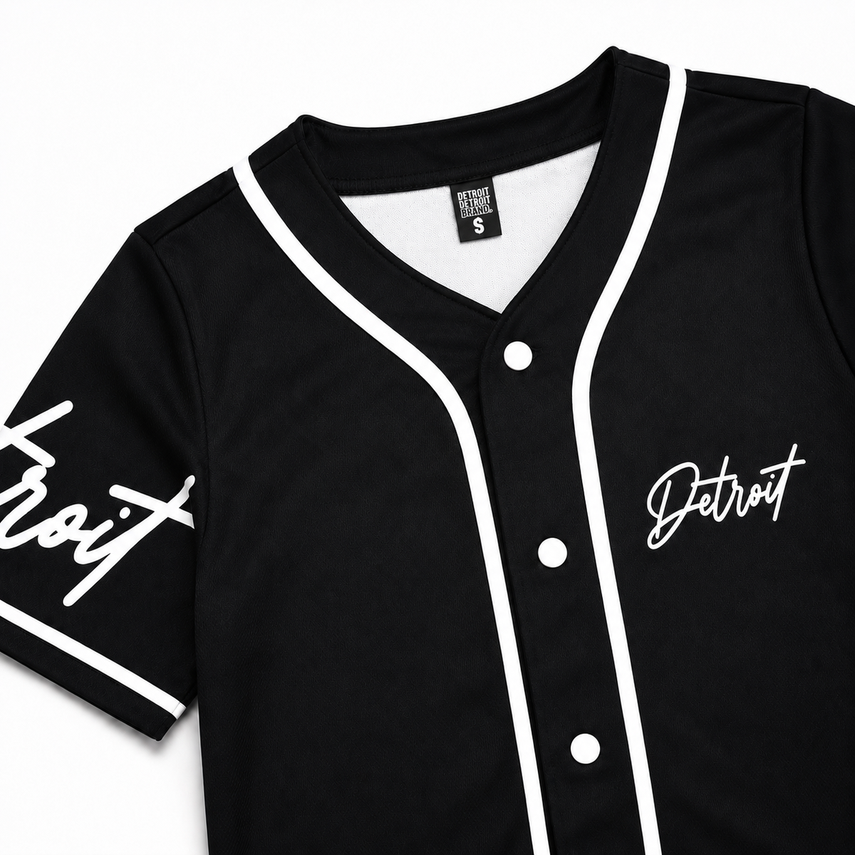 Close-up detail of a black Detroit baseball jersey with white piping, white interior neckline, Detroit Detroit Brand neck label, white buttons, and Detroit script graphics.