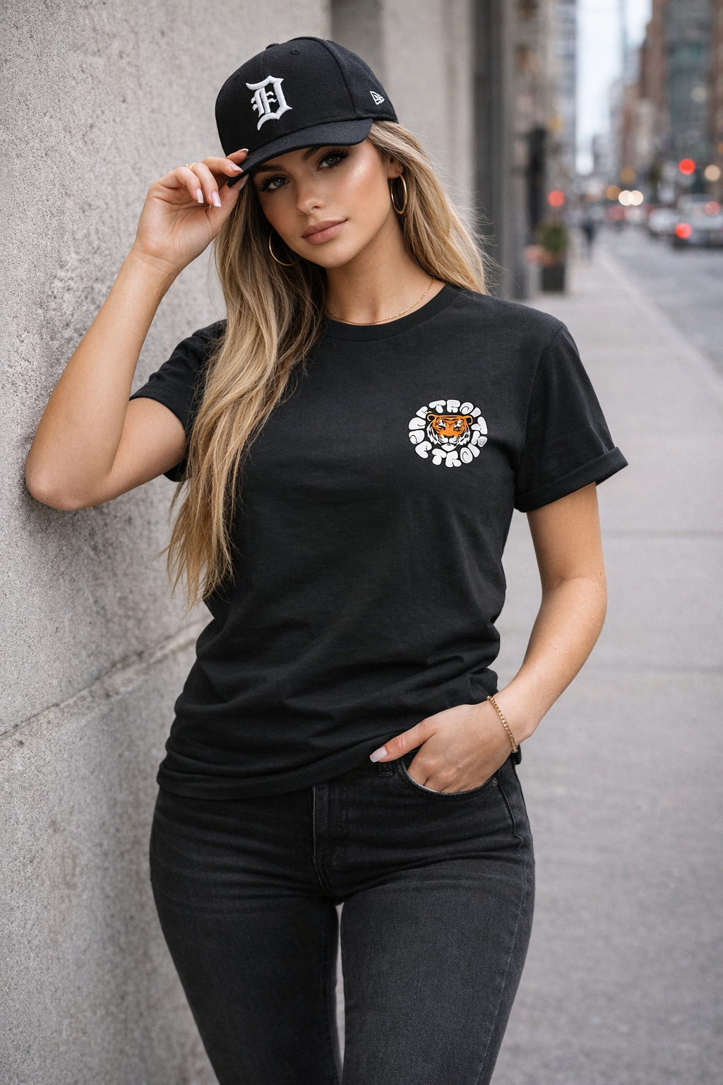 Urban female model wearing black Detroit tiger graphic t-shirt with skinny jeans and black Detroit D hat in city street setting
