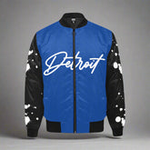 Blue Detroit bomber jacket with black sleeves featuring white paint-splatter design and bold white Detroit script on the front