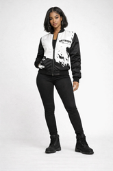 Brown-skinned female model wearing Detroit Born and Raised black and white splatter bomber jacket with black stretch pants and black boots in white studio setting
