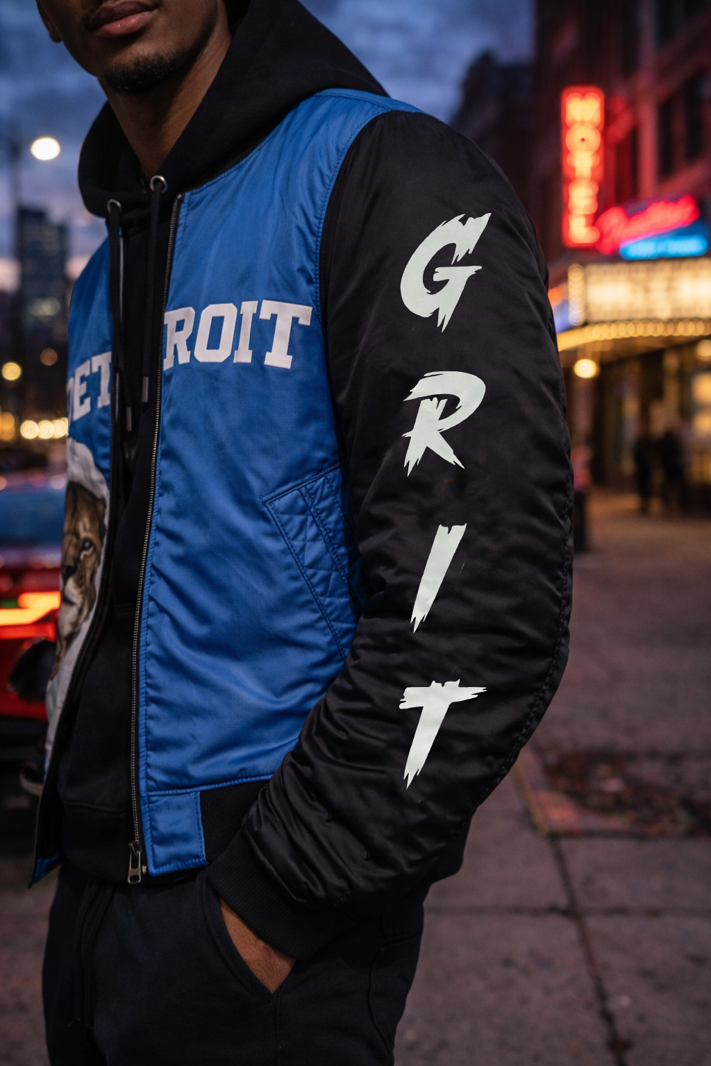 Person wearing a blue and black 'Lions' jacket with 'Detroit' and 'Grit' text, standing in an urban setting.