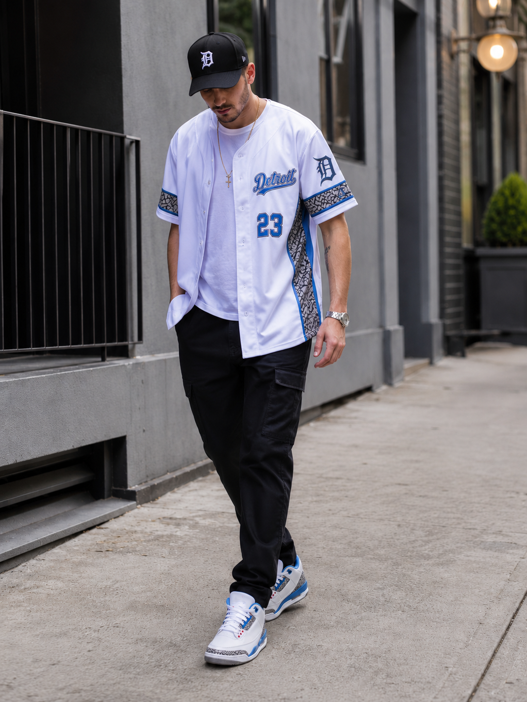 Male model walking through the city wearing the Detroit Heritage White & Blue Baseball Jersey styled with Air Jordan 3 True Blue sneakers for a modern Detroit-inspired look.