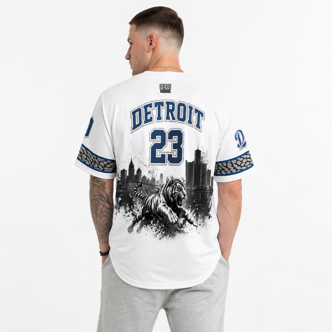 Rear view of a male model wearing the Detroit Heritage Baseball Jersey featuring Detroit lettering, number 23, Detroit skyline artwork, and roaring tiger graphic.