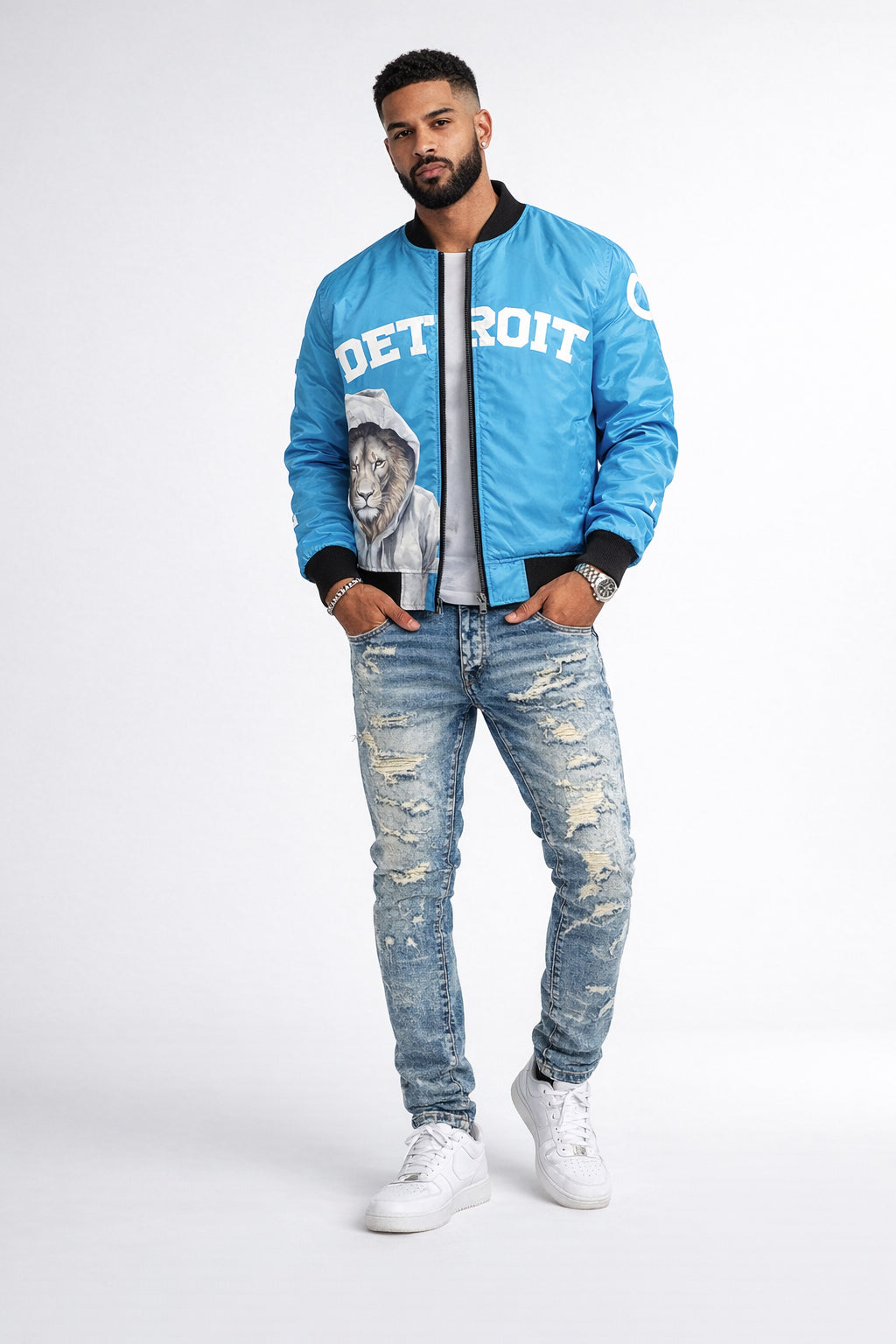 Man wearing a blue bomber jacket with 'Detroit' and a lion graphic, standing against a white background