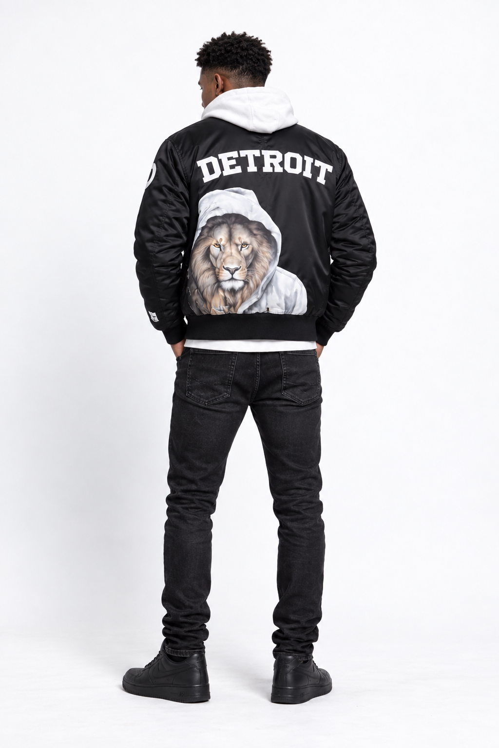 Back view of male model wearing black Detroit lion graphic bomber jacket with large hooded lion artwork and Detroit lettering