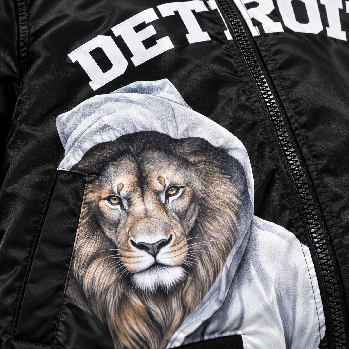 Close-up detail of black Detroit lion graphic bomber jacket featuring printed hooded lion artwork and white Detroit lettering