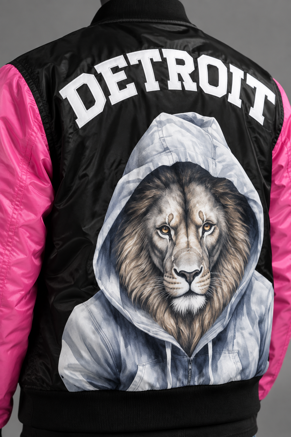 Close-up back detail of black and pink Detroit lion graphic bomber jacket featuring hooded lion artwork and white Detroit lettering