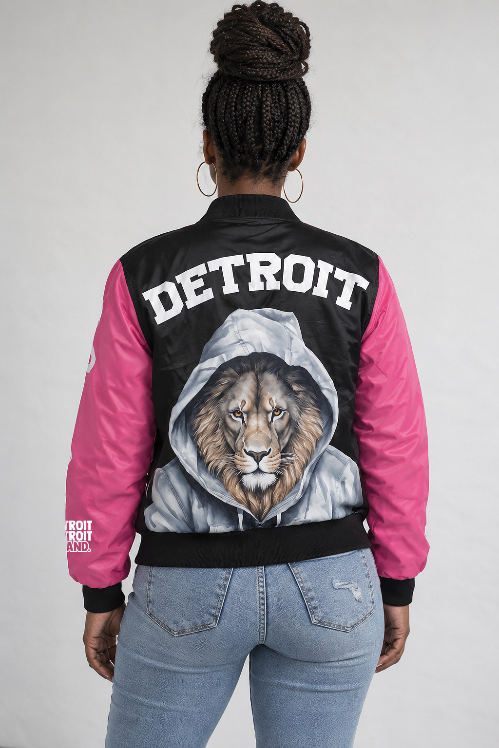 Back view of woman wearing Detroit Lions pink bomber jacket with large hooded lion artwork and white Detroit lettering
