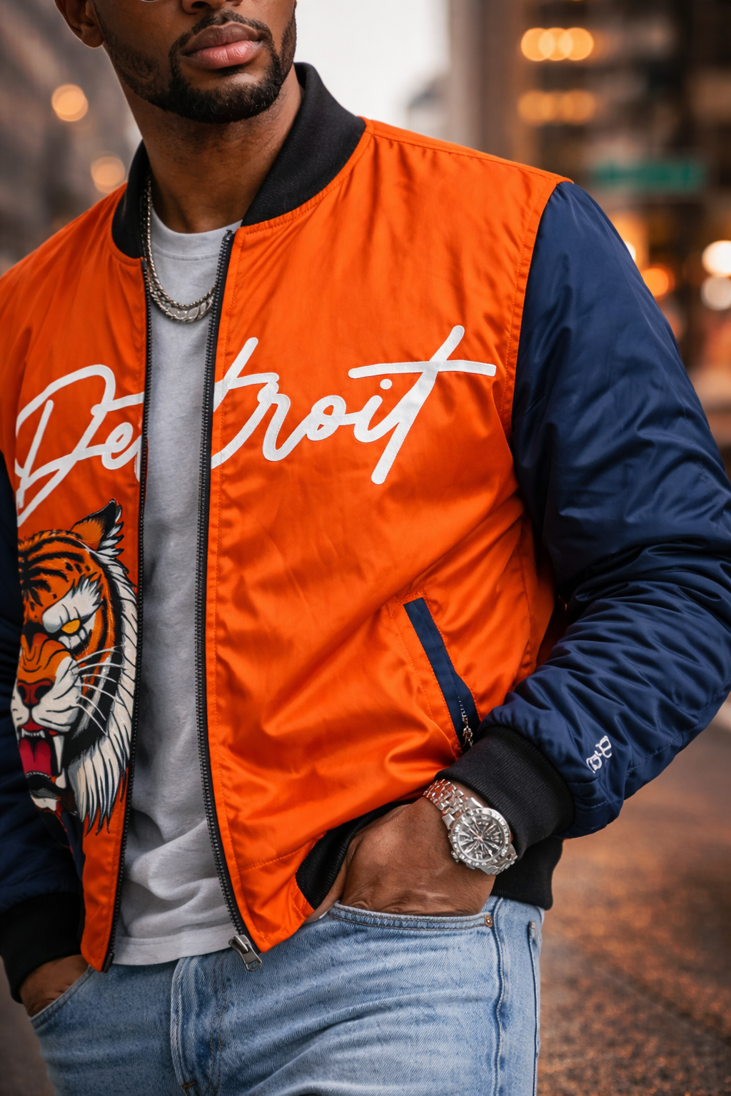 Person wearing an orange and navy jacket with 'Detroit' and a tiger design, standing in an urban setting.