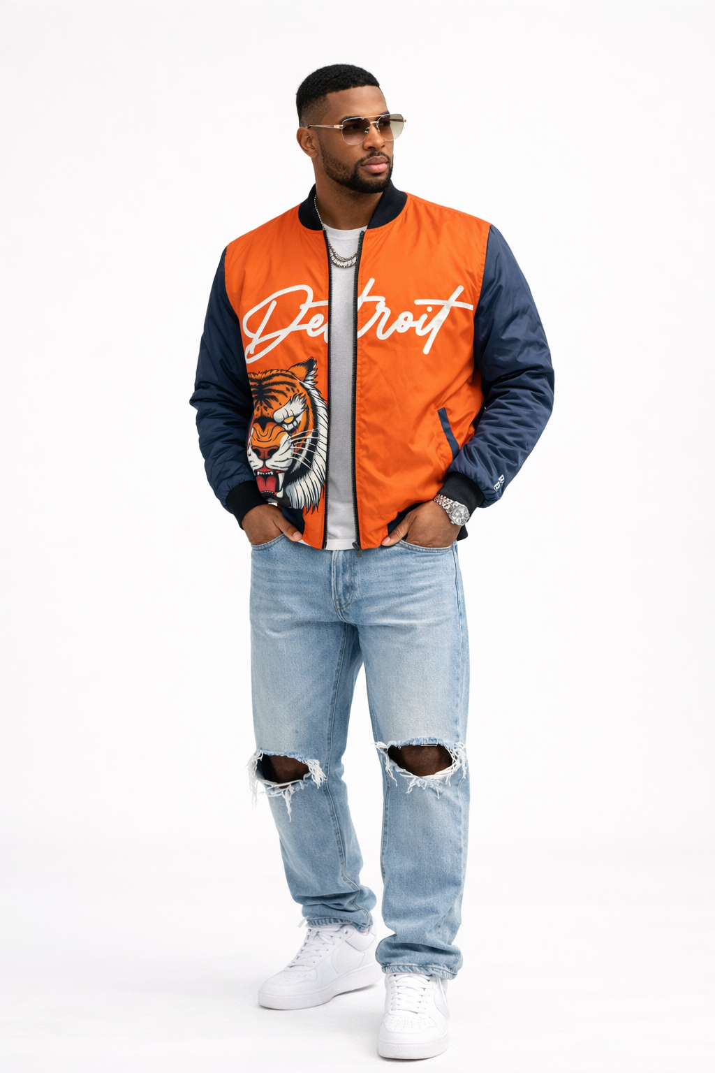 Man wearing an orange and navy jacket with a tiger design and 'Detroit' text, paired with ripped jeans on a white background.