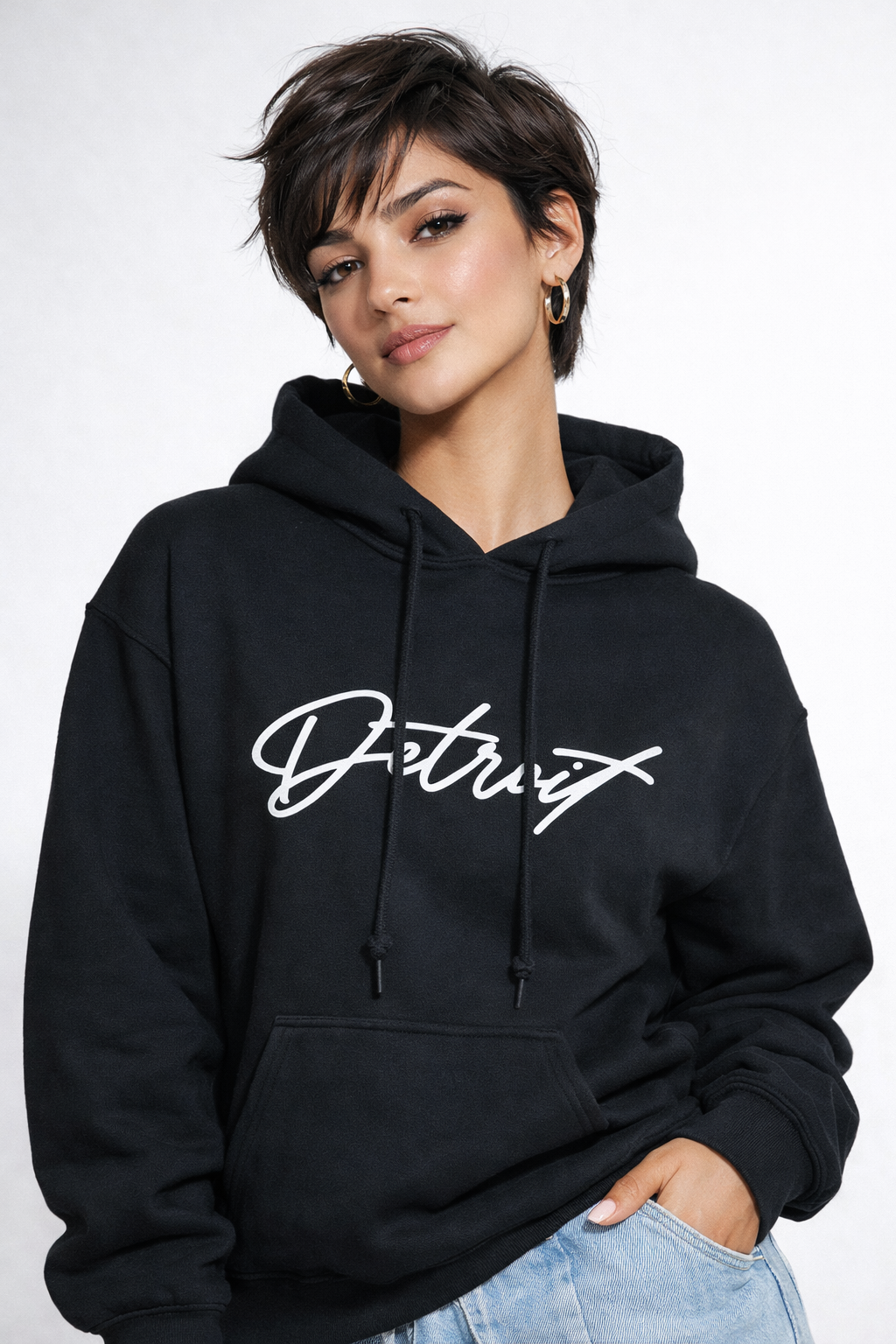 Woman wearing black Detroit script hoodie front view with relaxed fit, styled with light denim jeans, minimal studio background