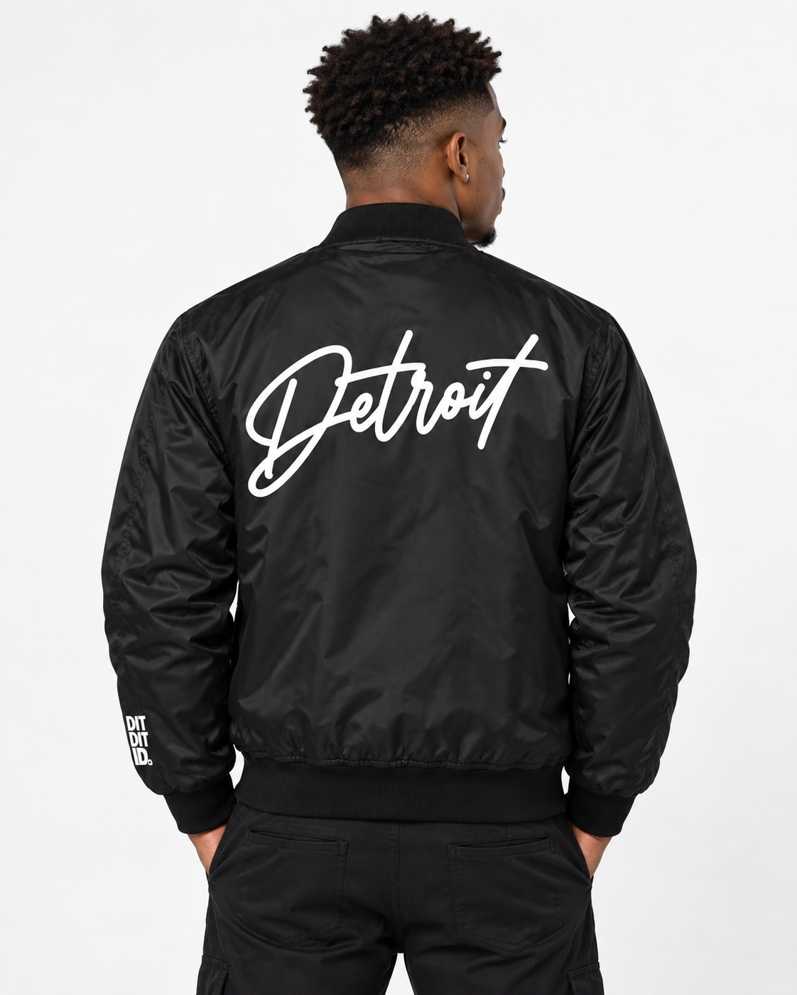 Male model wearing black Detroit bomber jacket with large white Detroit script on back
