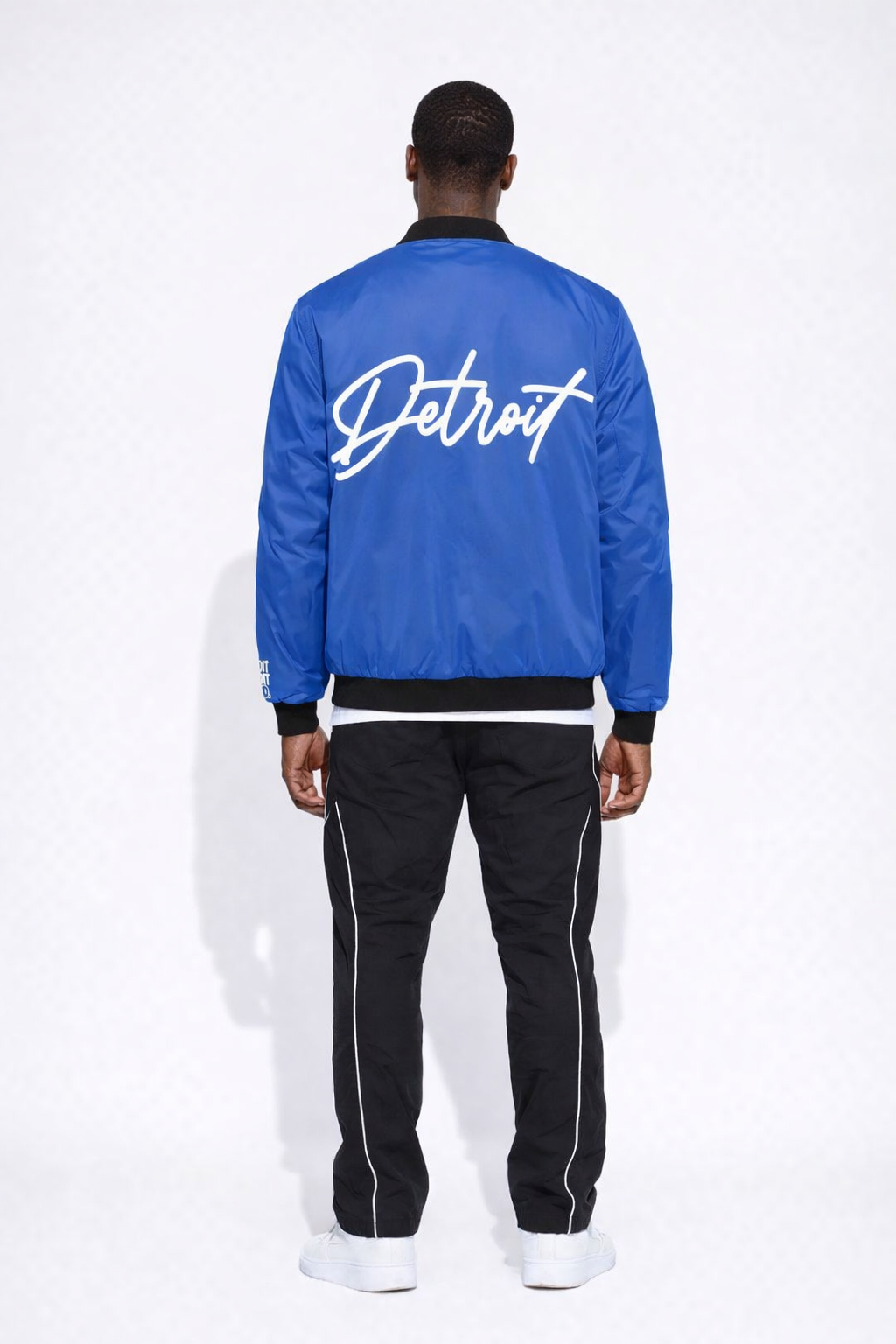 Person wearing a royal blue jacket with 'Detroit' text on the back, standing against a white background