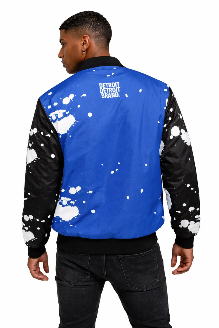 Back view of brown skin male model wearing Detroit Splatter Bomber Jacket showing Detroit Detroit Brand logo with paint splatter design on white background