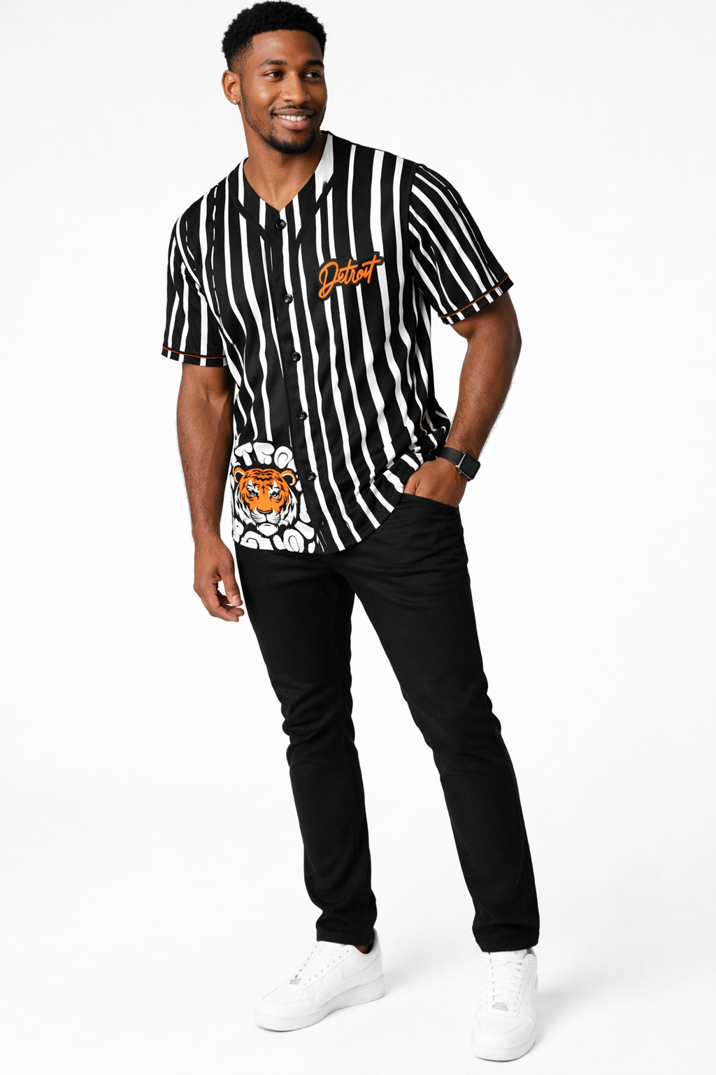 Full body front view of a male model wearing a black and white striped Detroit baseball jersey with orange script logo, paired with black pants and white sneakers on a clean white studio background