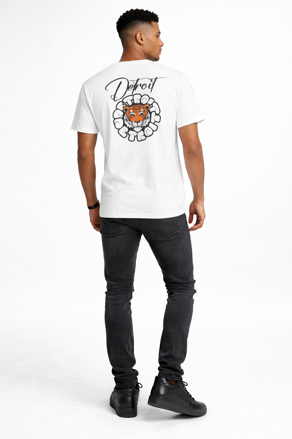 Back view of male model wearing Detroit tiger graphic t-shirt with large Detroit print on back, distressed black jeans and black Nike Air Force 1 sneakers on white background