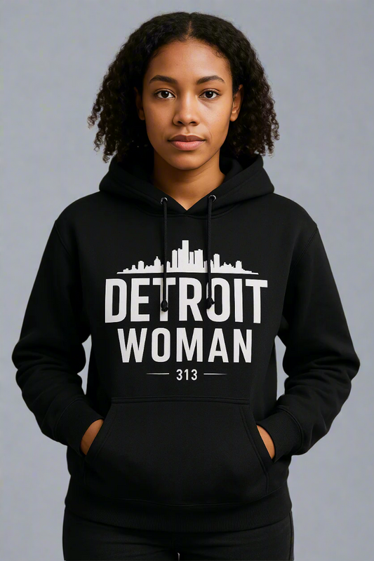Woman wearing a black hoodie with white text that reads “Detroit Woman 313” and a city skyline graphic above the text, standing against a plain gray background.