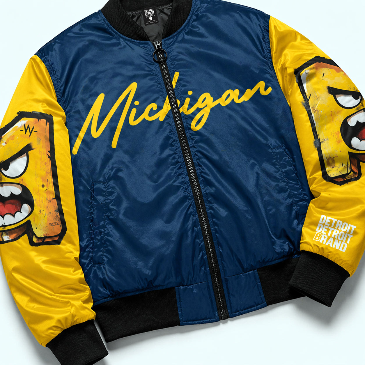 Flat lay detail of Michigan National Champions 2026 bomber jacket showing fabric texture, zipper, and sleeve artwork in navy and maize