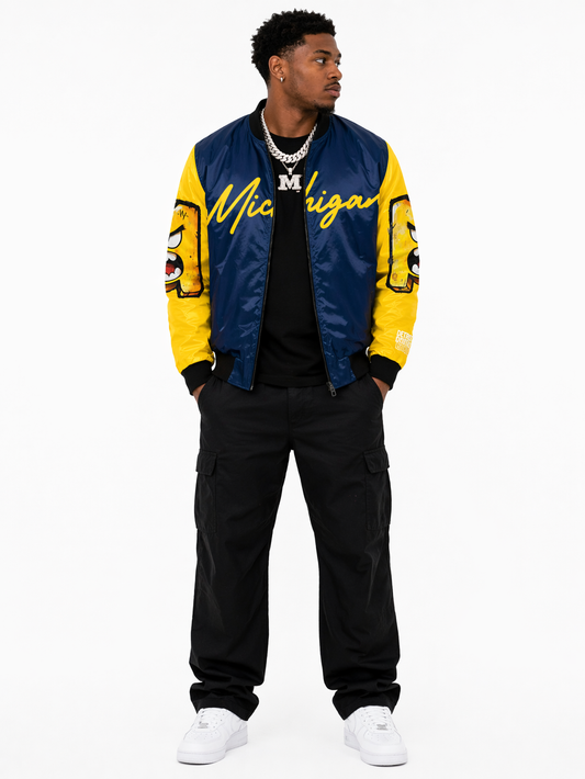 Male model wearing Michigan National Champions 2026 bomber jacket front view with silver chains, premium Detroit streetwear varsity jacket navy and yellow