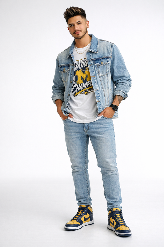 Full body studio photo of a male model wearing a Michigan championship graphic t-shirt with a light denim jacket and jeans, styled with a thick gold chain necklace and navy yellow sneakers on a white background.