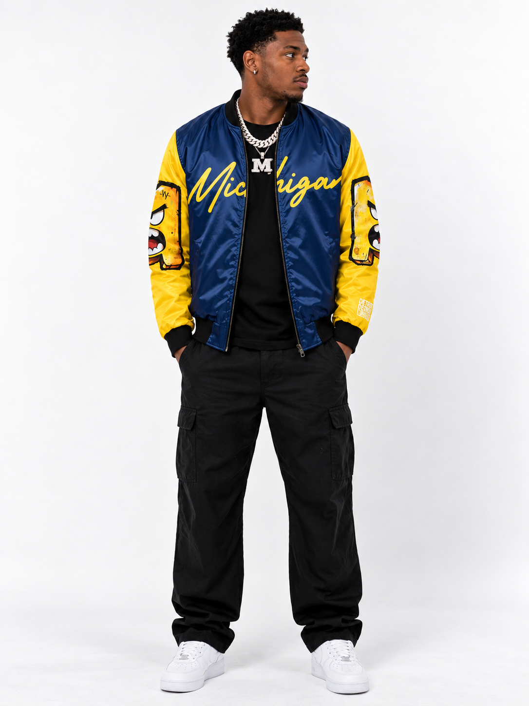         Black male model wearing the Michigan Illustrated Bomber Jacket in blue and maize with bold Michigan script and graphic illustrated sleeves.